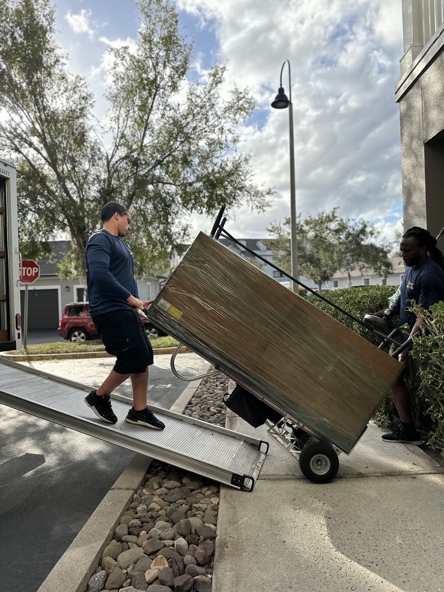 Movers guiding a dresser down the ramp on a dolly